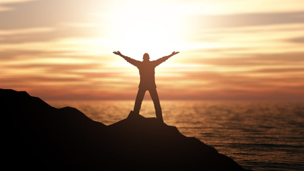 man with arms raised in front of sunset